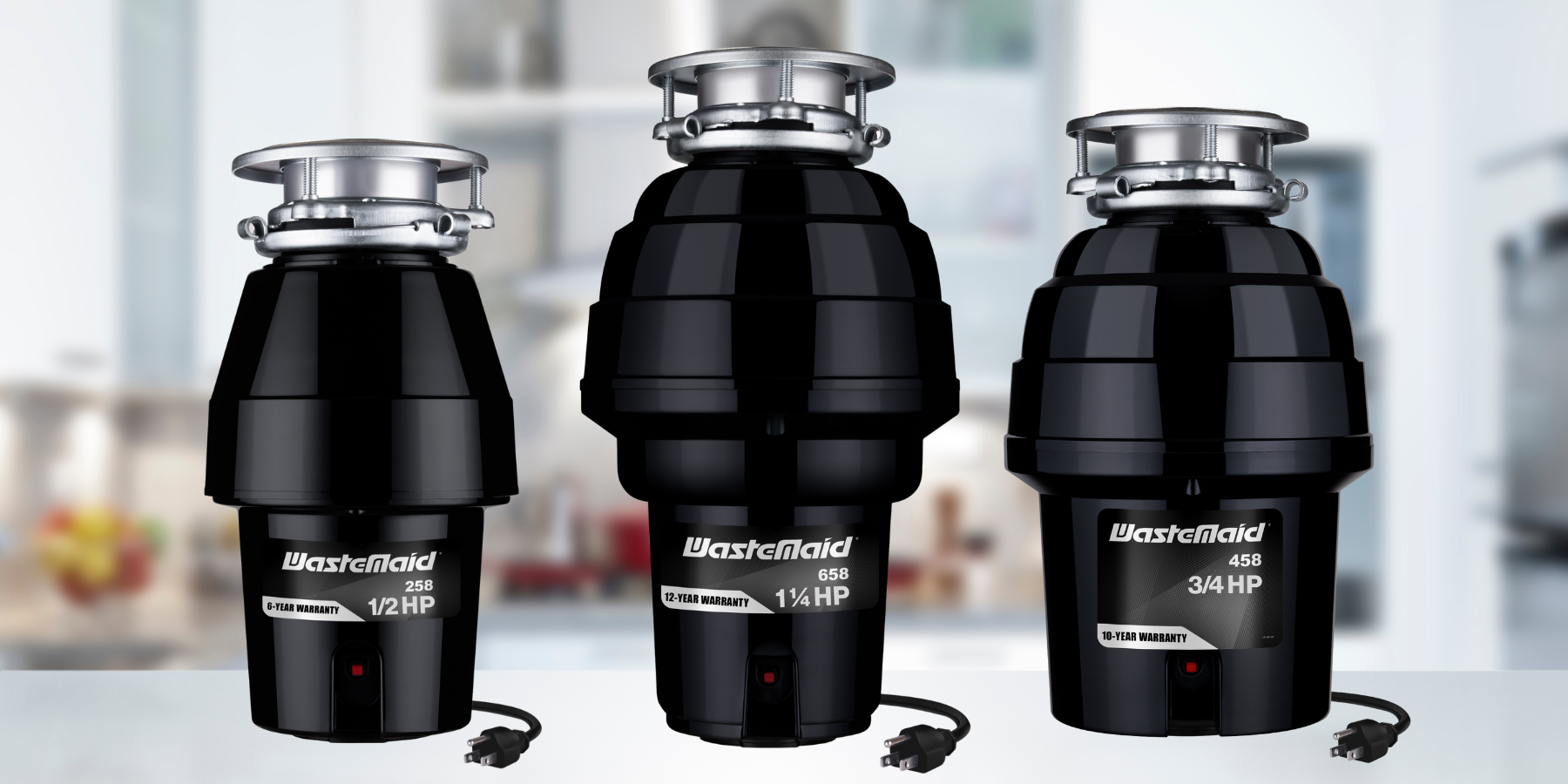 Three WasteMaster garbage disposals on a kitchen counter with a blurred kitchen background.